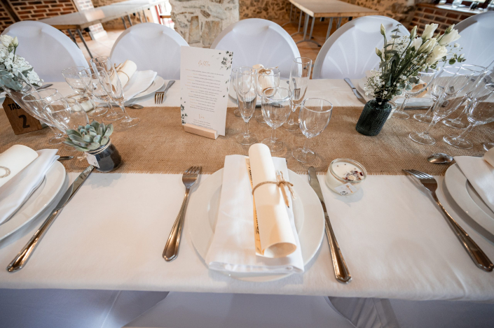 Table de mariage avec chemin de table en jute Table de mariage avec chemin de table en toile de jute, menu sur support en bois, plante grasse et serviette roulée nouée de ficelle
