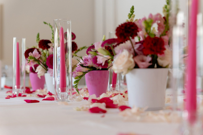 Décoration de table de mariage rose fuchsia : bougies flambeaux dans des vases tubes, pots de fleurs roses et pétales de roses