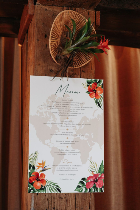 Menu de mariage tropical suspendu Menu de mariage au thème tropical à motifs d'hibiscus, suspendu à une poutre en bois avec un éventail en rotin