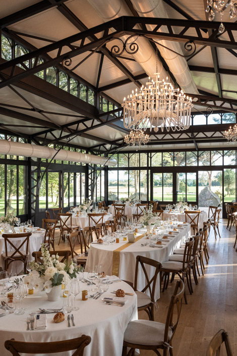 Salle de mariage sous verrière Salle de mariage sous verrière avec lustre en cristal, tables rondes dressées et chaises en bois
