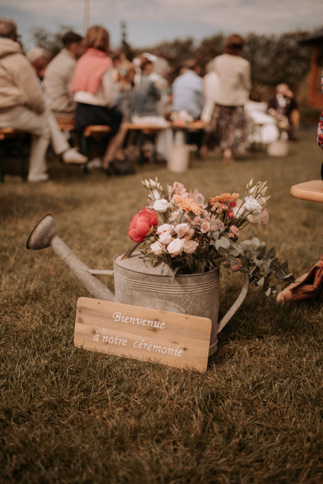 Arrosoir en zinc fleuri et panneau en bois « Bienvenue à notre cérémonie » pour une cérémonie laïque en extérieur
